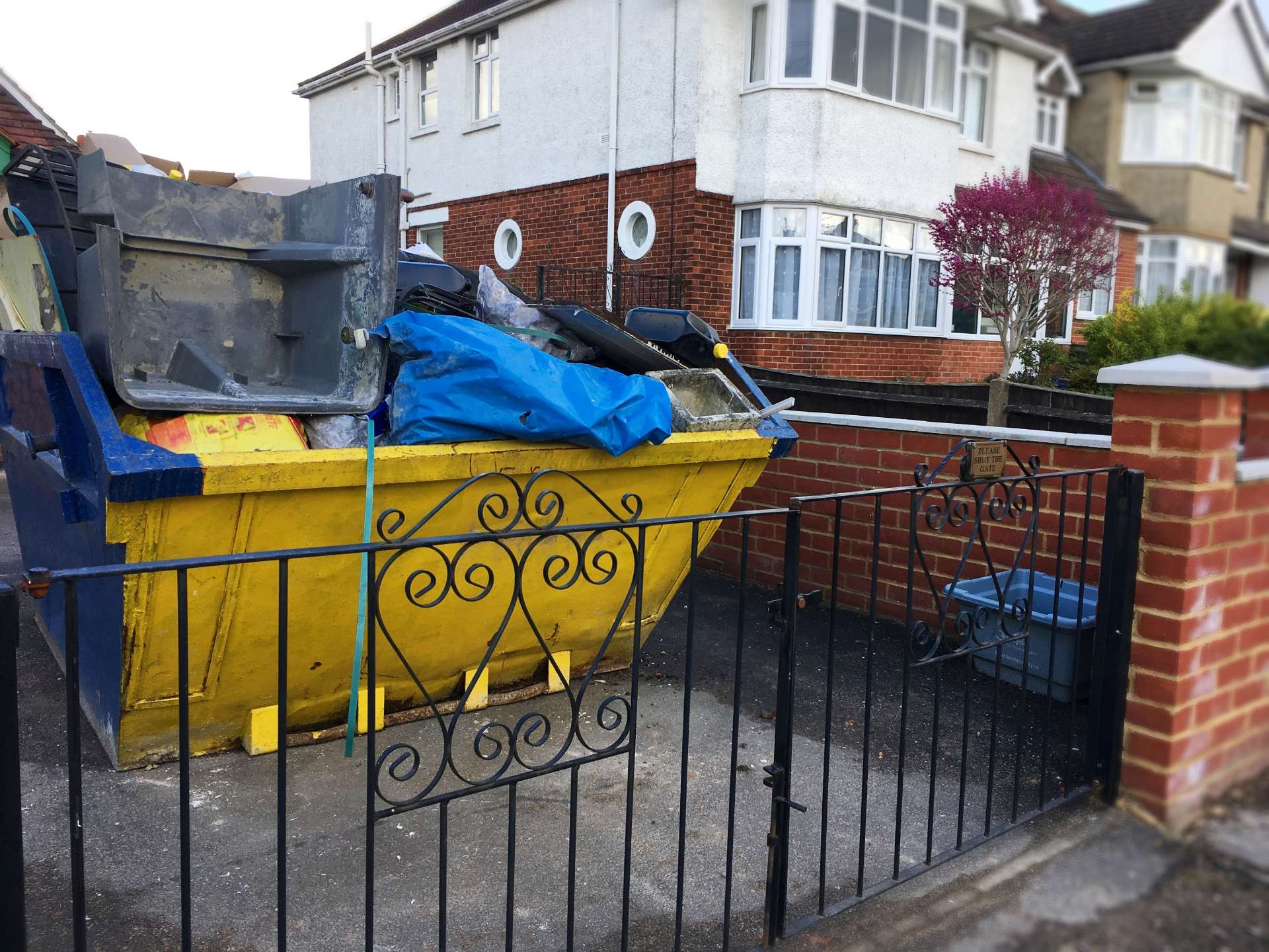 Overfilled skip by fence in residential area.