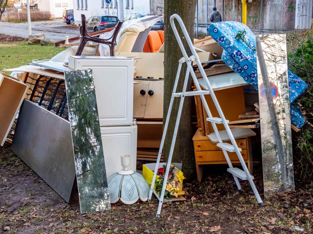 Discarded furniture, mirrors, and a ladder outside.